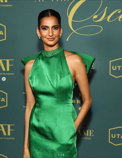 Woman in emerald green satin halter dress posing at a formal event against a dark teal backdrop