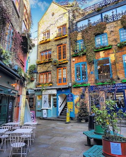 Colorful brick buildings with green plants and blue windows surrounding a small courtyard in Neal's Yard, London
