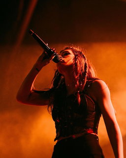 Woman singing into a microphone on stage with orange lighting