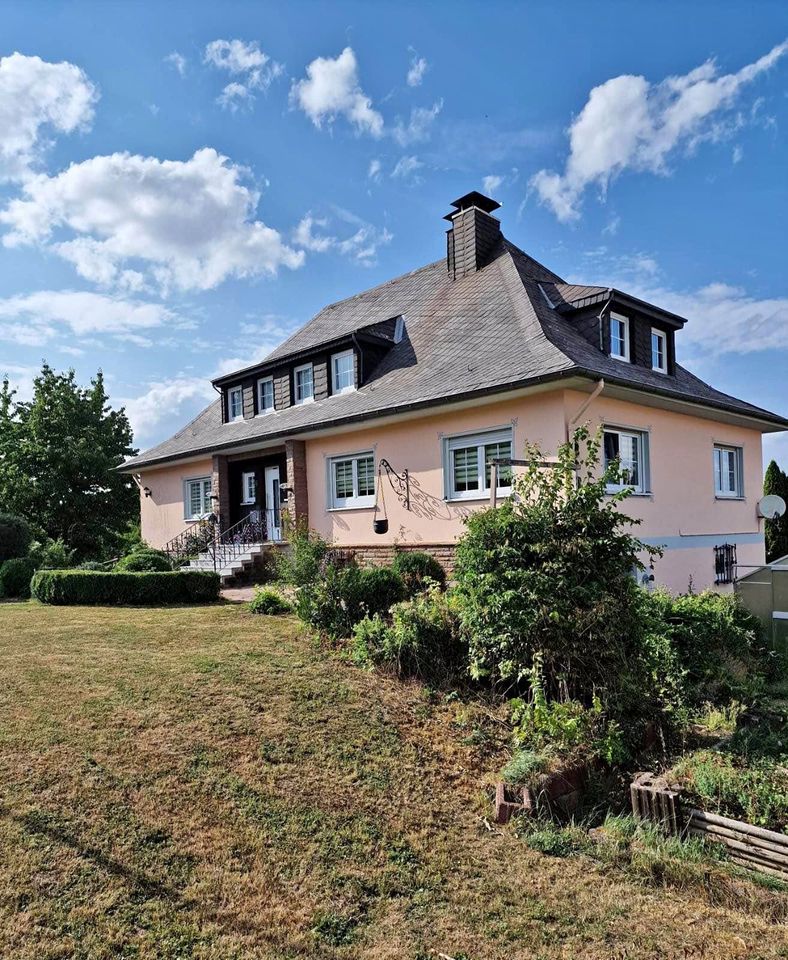 Peachy-pink European house with gray mansard roof on hillside lawn under blue sky with white clouds
