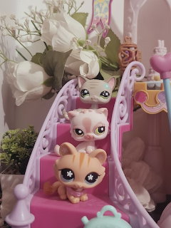 Three LPS cat toy figures on a pink staircase with white flowers behind them