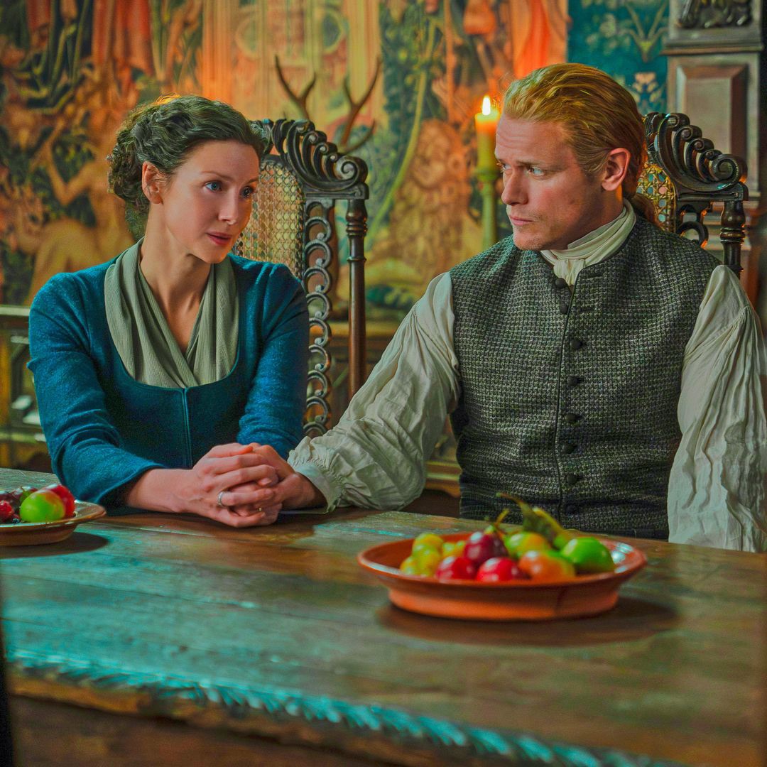 Man and woman in period costume seated at wooden table with fruit bowls in historic room