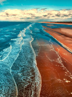 Turquoise ocean waves meeting golden sandy beach with cloudy sky above