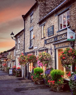 Stone village shop with hanging flower baskets on cobblestone street at sunset