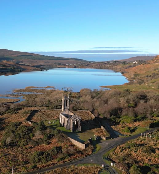 Small stone church beside a lake with hills and clear blue sky