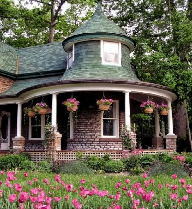 Victorian brick cottage with turret and porch surrounded by blooming pink tulips