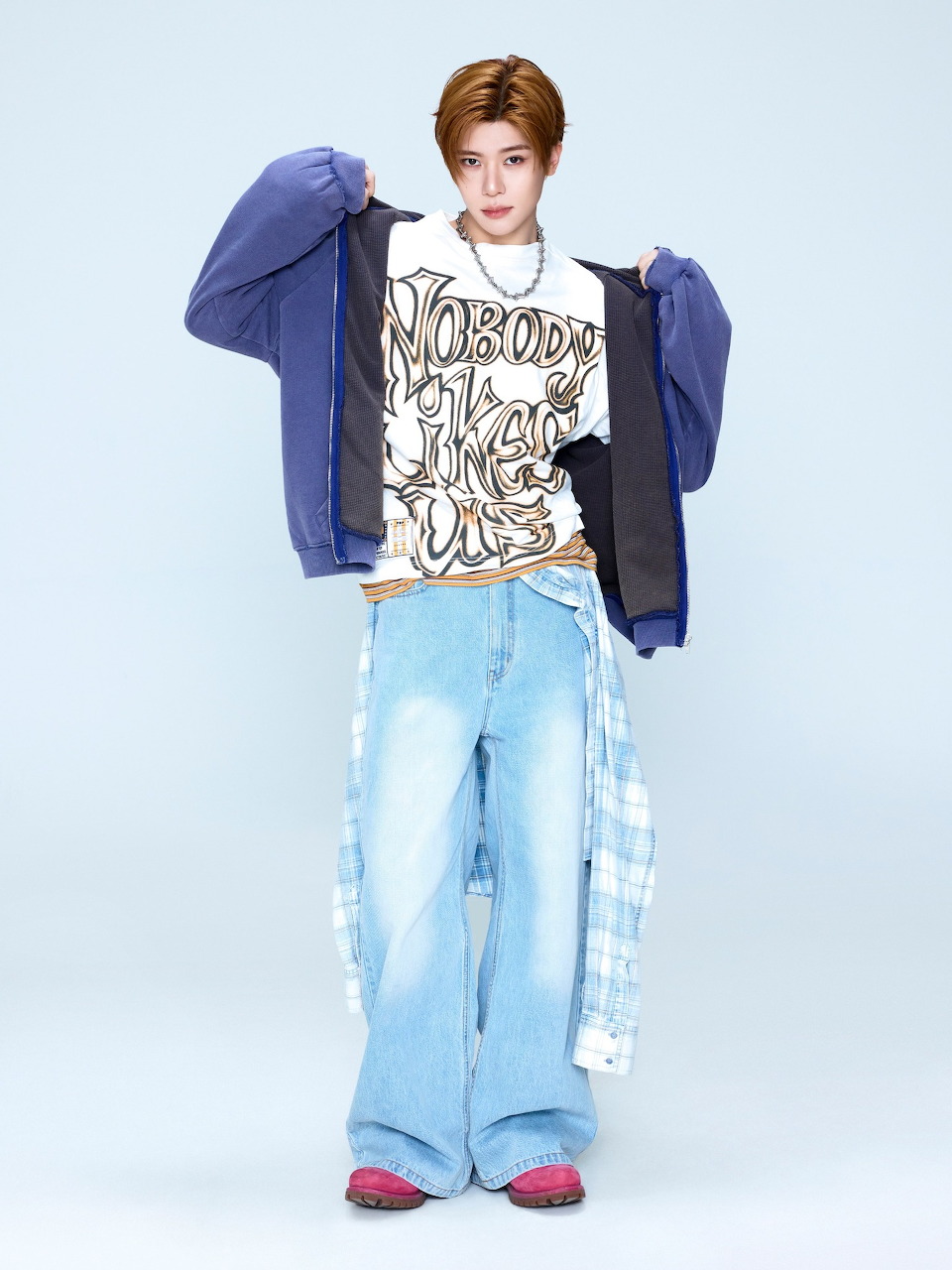 Young man in streetwear outfit with wide-leg jeans, graphic tee, and blue jacket on light blue background