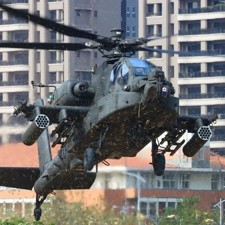 Military Apache helicopter flying in front of high-rise buildings