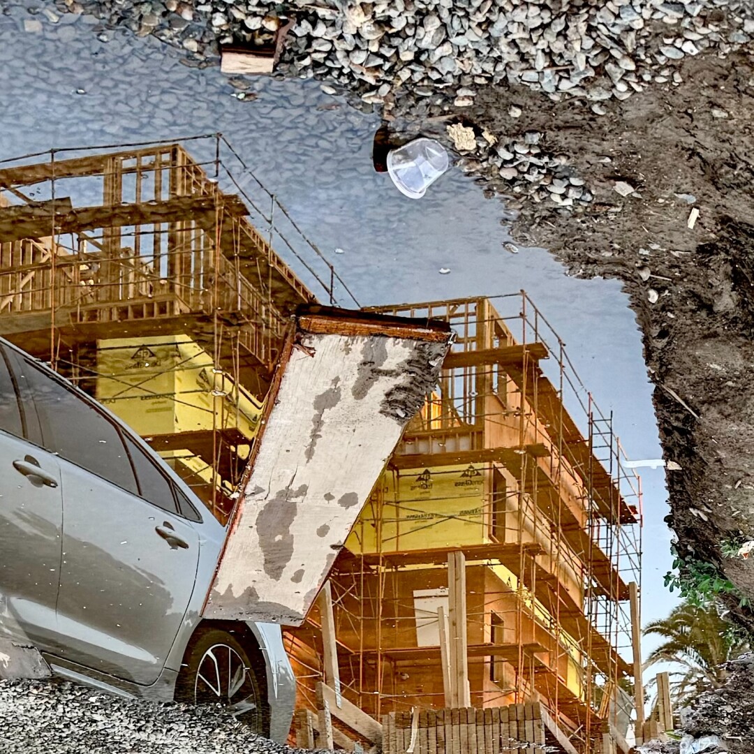 Construction site and car reflected in a muddy puddle beside gravel