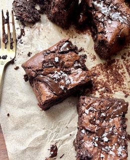 Chocolate brownies with sea salt on parchment paper next to a gold fork