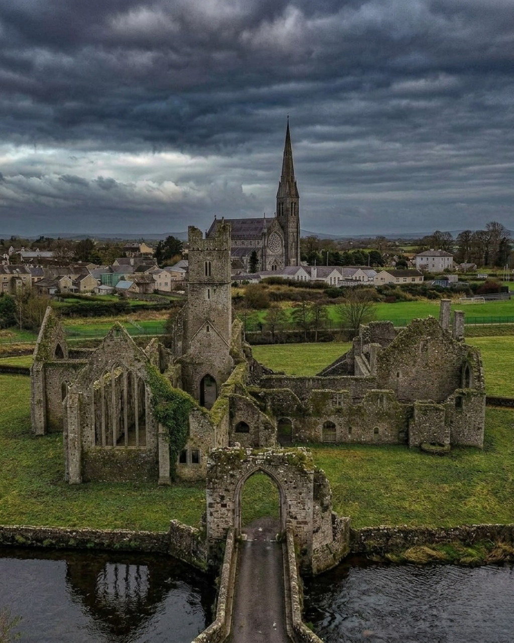 Aerial view of St. Saviour's Priory ruins in Kilmallock, Ireland, with a church spire and village beyond