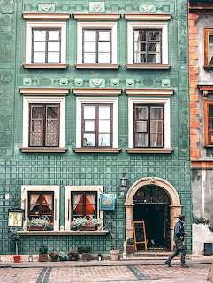 Green tiled building facade with ornate windows and arched doorway on a coblestone street