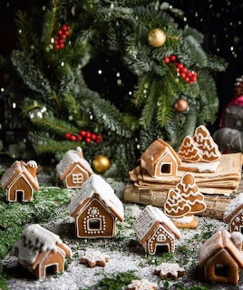Miniature gingerbread houses and trees with white icing arranged as a Christmas village with powdered sugar snow