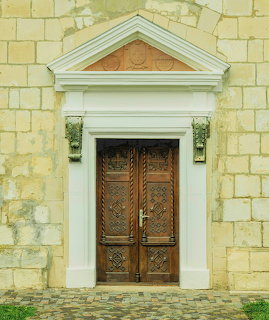 Ornate carved wooden double door with white classical pediment in yellow stone wall
