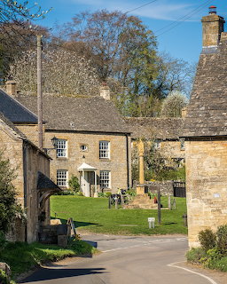 Stone cottages with chimneys along a village road with grass and trees