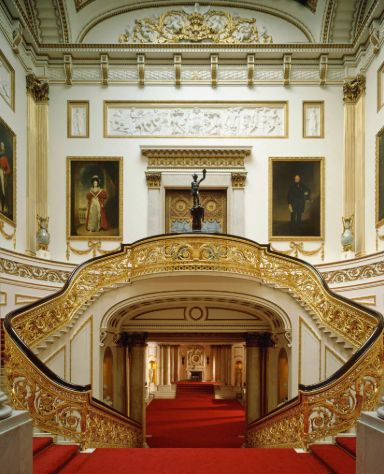 Grand gilded staircase inside Buckingham Palace with red carpet and ornate gold railings