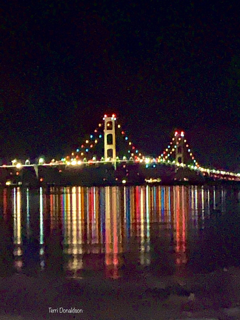 Colorfully lit suspension bridge at night with reflections in the water