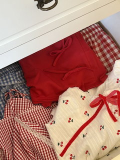 Red and white summer clothes including gingham and cherry print folded in a white drawer
