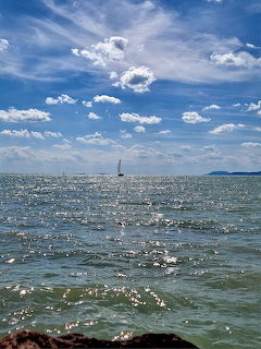 Sunlit lake water with sailboat under cloudy blue sky