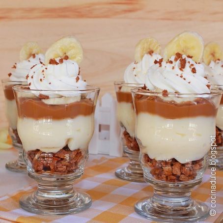 Two layered banana pudding parfaits in glass cups topped with whipped cream, banana slices, and chocolate shavings