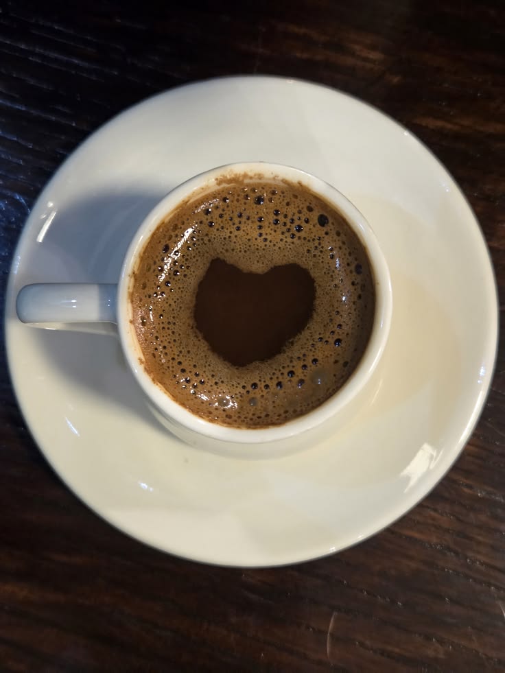 Cup of Turkish coffee with foam on white saucer, viewed from above on wooden surface