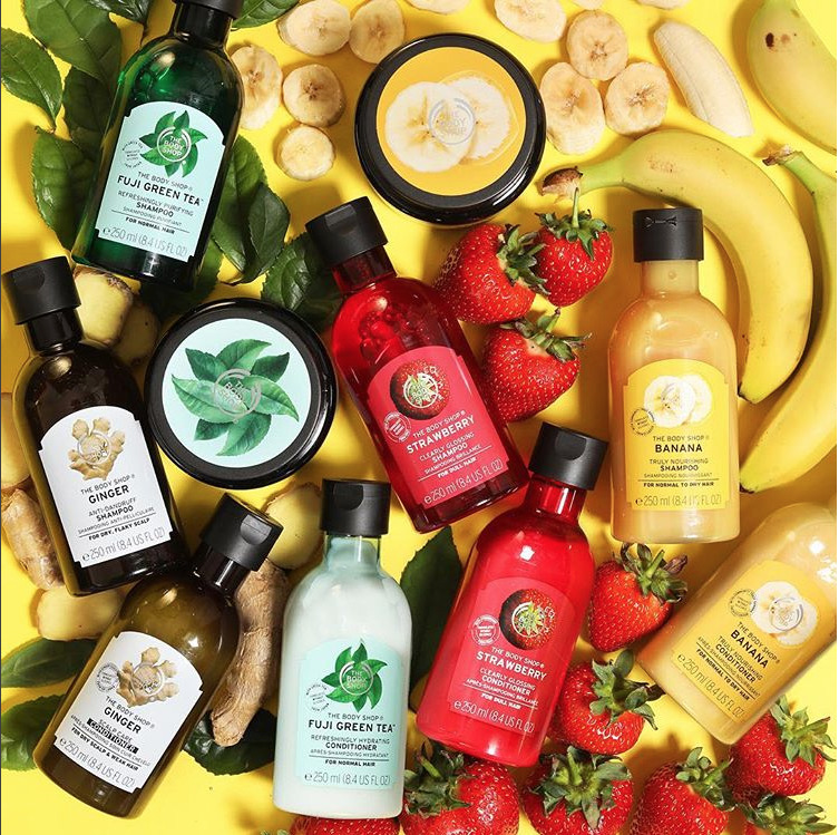 Bottles and jars of body care products surrounded by bananas, strawberries, and citrus on yellow
