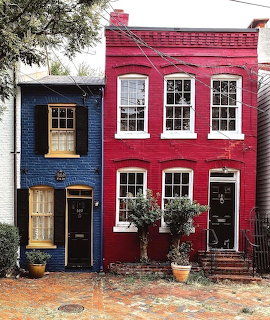 A narrow navy blue house next to a bright red house with white window frames and potted plants
