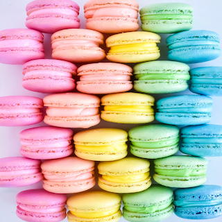 Stacked pastel macarons in pink, peach, yellow, green, and blue on a light background