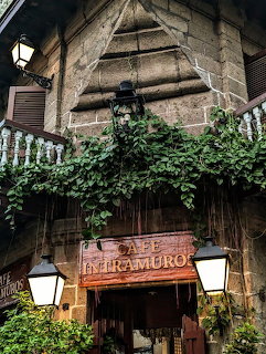 Stone building entrance with Cafe Intramuros sign, green vines, lanterns, and iron balcony