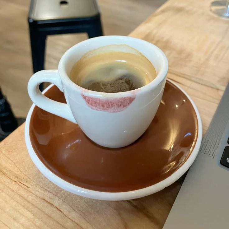 White espresso cup with a lipstick mark on a brown saucer on a wooden table