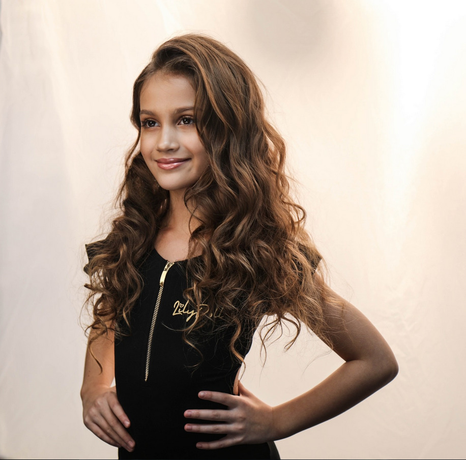 Young girl with long curly brown hair in black top smiling at camera