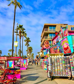 Colorful Venice Beach boardwalk with vendor stalls, palm trees, and blue sky