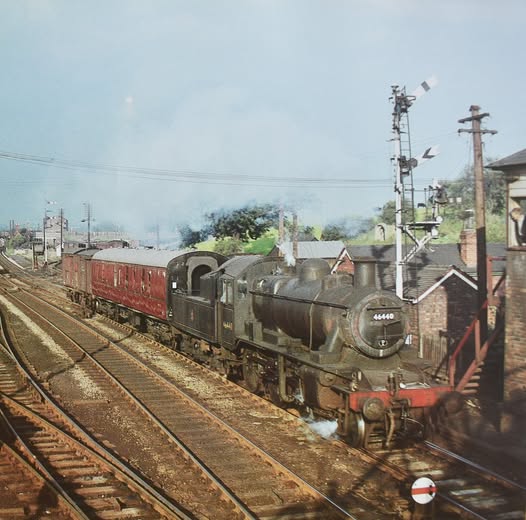Vintage steam locomotive with freight cars on railway tracks near industrial buildings and signal towers