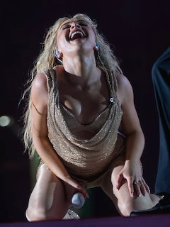 Blonde woman in gold dress laughing on stage during concert performance