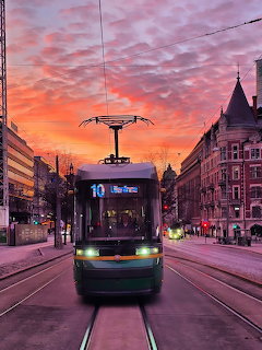 Green tram on Helsinki street under vivid pink and orange sunset sky with historic architecture