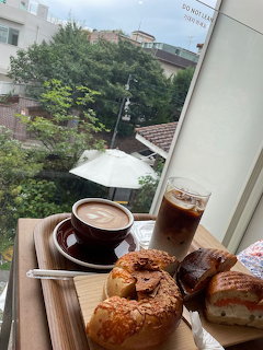 Latte, iced coffee, and pastries on a tray by a window overlooking trees and nearby buildings.