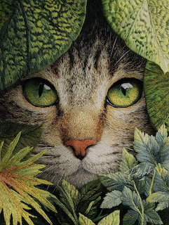 Close-up of a tabby cat peeking through green leaves with bright green eyes