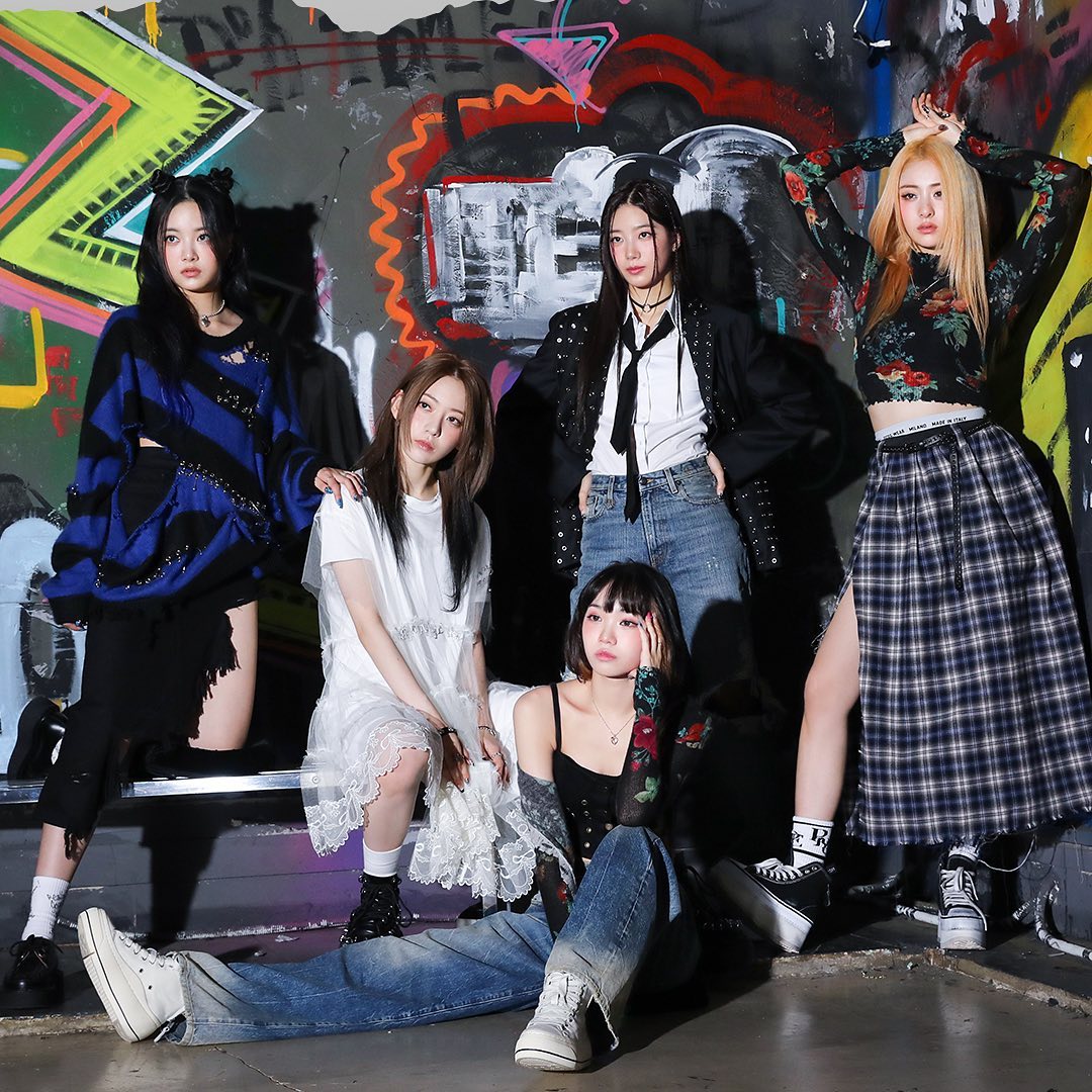Five young women in street fashion posing against colorful graffiti wall
