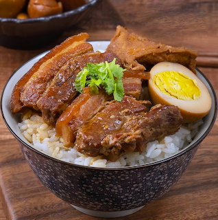 Bowl of rice topped with braised pork belly, soft-boiled egg half, and green garnish on wooden surface
