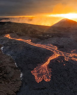 Glowing lava flow across a dark volcanic landscape at sunset