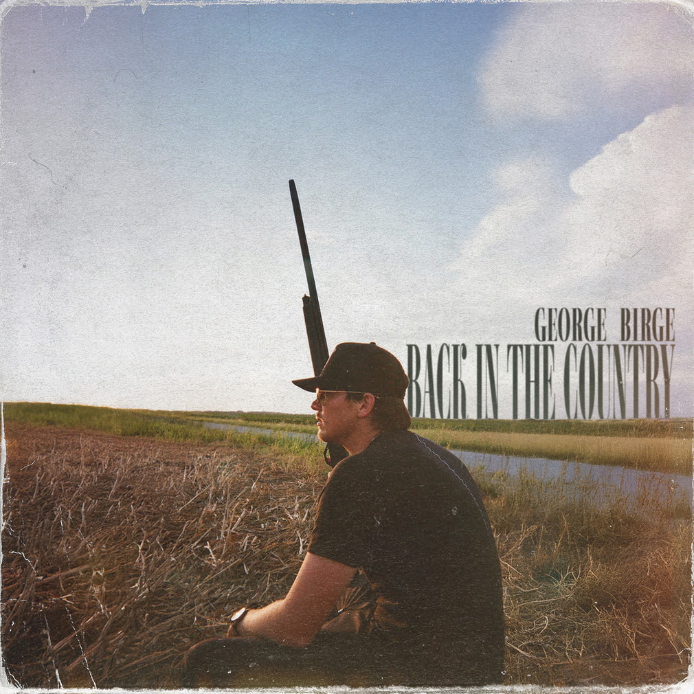Man in a black cap sitting in a dry field beside water under a cloudy sky with George Birge text