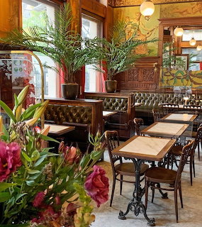 Ornate vintage brasserie interior with marble tables, leather seating, wood paneling, and fresh flowers