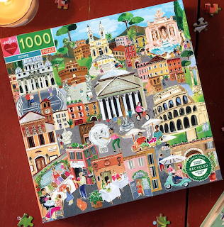 Illustrated Rome landmark collage on a square puzzle box with loose puzzle pieces on a wooden table