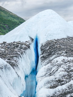Deep blue crevasse in Matanuska Glacier ice with green Alaskan hills in background
