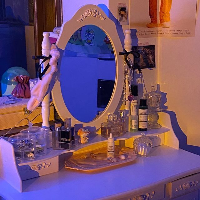 White vanity table with oval mirror, perfume bottles and cosmetics under purple lighting