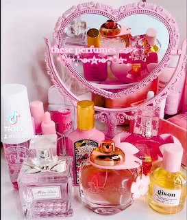 Pink heart-shaped mirror surrounded by various perfume bottles on a feminine vanity setup