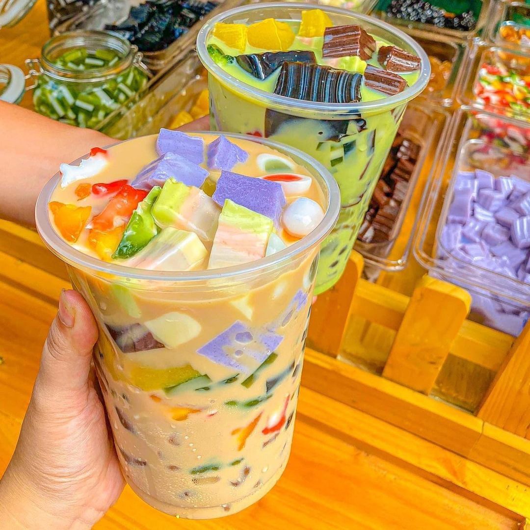 Hand holding a colorful Thai milk tea with jelly and fruit toppings in a plastic cup