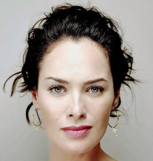 Close-up portrait of Lena Headey with dark hair and hoop earrings against a plain background