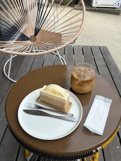 Slice of layered yuzu cake on white plate with iced coffee on outdoor cafe table