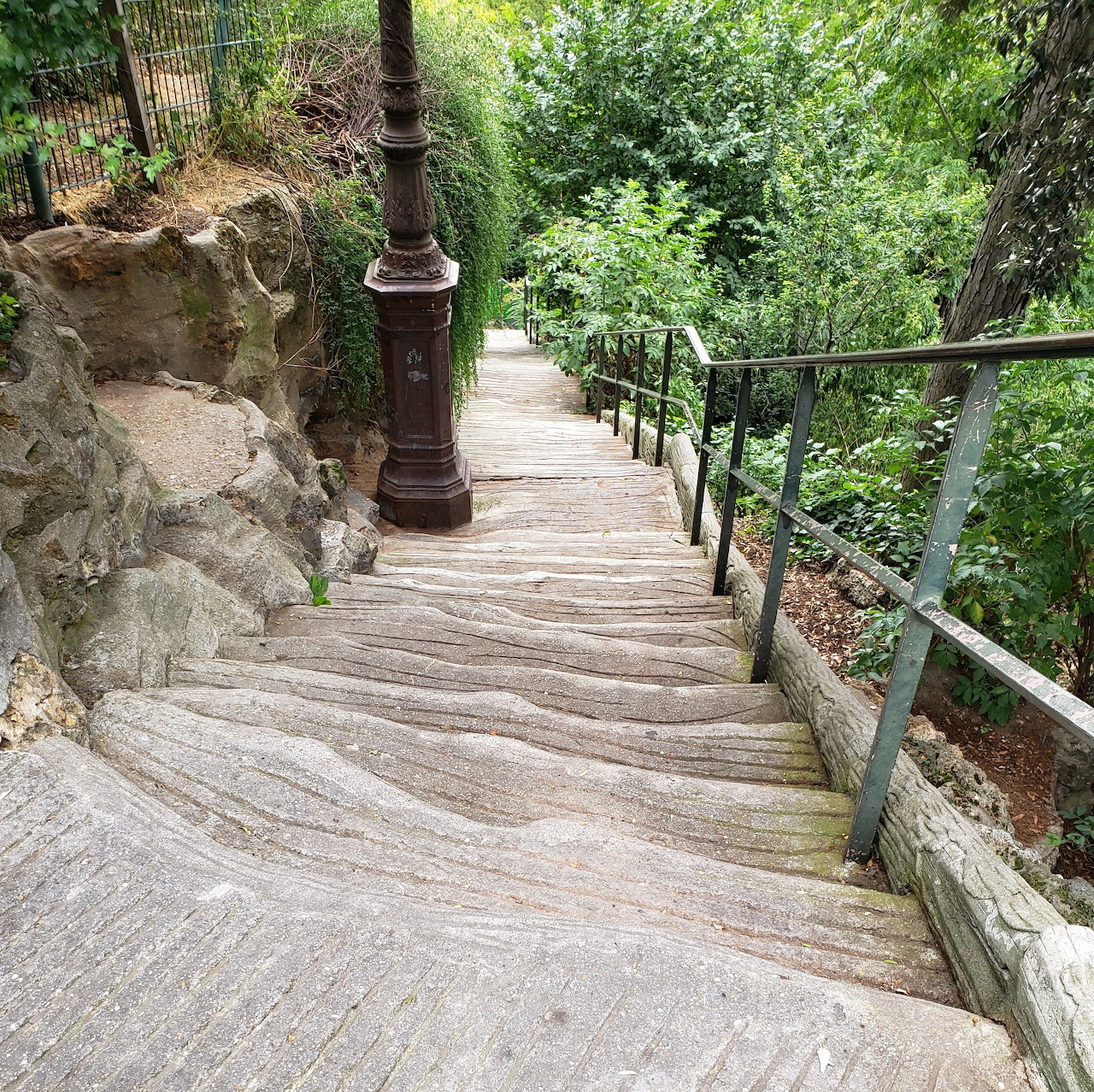 Stone staircase with black railing descending through green garden foliage in Paris